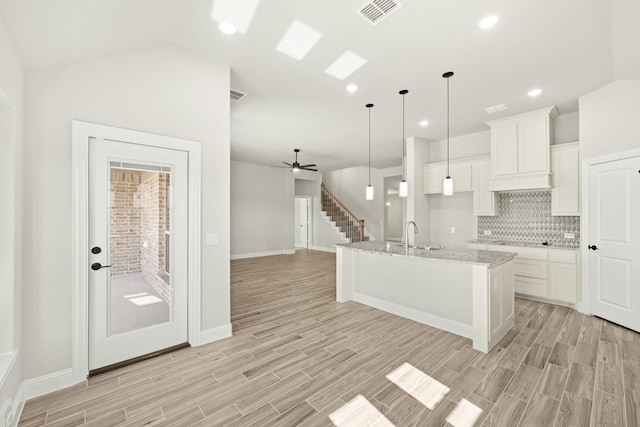 kitchen featuring vaulted ceiling, white cabinets, pendant lighting, a kitchen island with sink, and backsplash