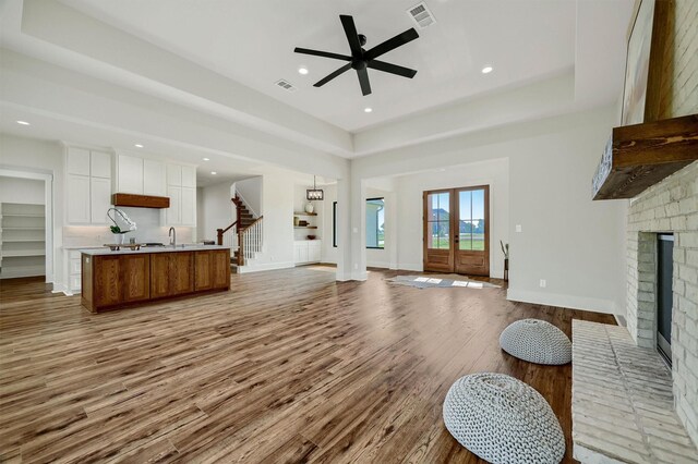 living room with light wood-type flooring, a brick fireplace, sink, ceiling fan, and a tray ceiling