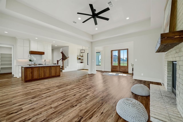 living room with sink, a fireplace, a raised ceiling, and light wood-type flooring