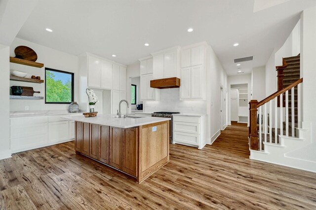 kitchen featuring a kitchen island with sink, stainless steel gas range, white cabinetry, sink, and light hardwood / wood-style floors