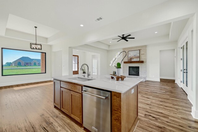 kitchen featuring a raised ceiling, decorative light fixtures, a fireplace, an island with sink, and sink