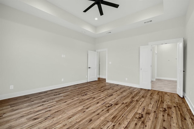 unfurnished bedroom with ceiling fan, wood-type flooring, and a raised ceiling