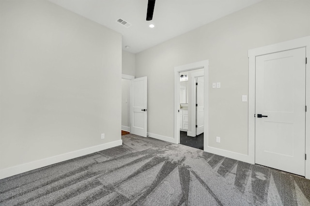 unfurnished bedroom with ensuite bath, ceiling fan, and dark colored carpet