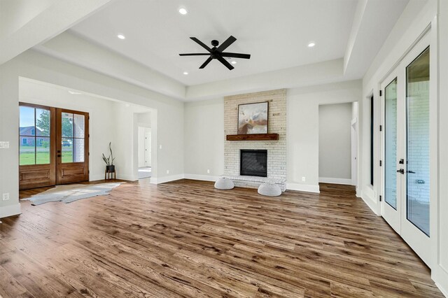 unfurnished living room with hardwood / wood-style flooring, a fireplace, french doors, a tray ceiling, and ceiling fan