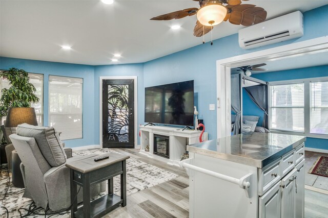 living room with an AC wall unit, light wood-type flooring, and ceiling fan