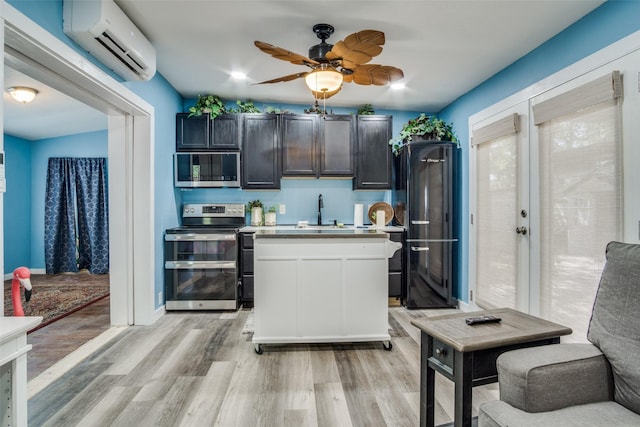 kitchen with an AC wall unit, light wood-type flooring, sink, ceiling fan, and appliances with stainless steel finishes