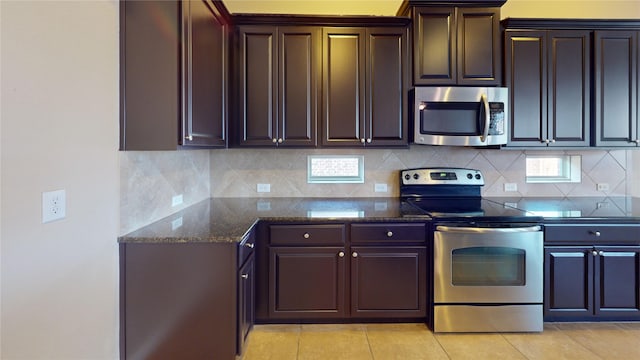 kitchen with tasteful backsplash, dark brown cabinetry, dark stone countertops, appliances with stainless steel finishes, and light tile patterned floors