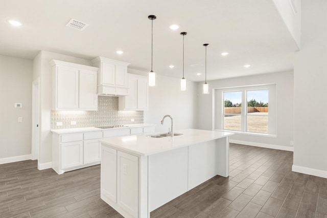 kitchen featuring light countertops, pendant lighting, white cabinets, and an island with sink