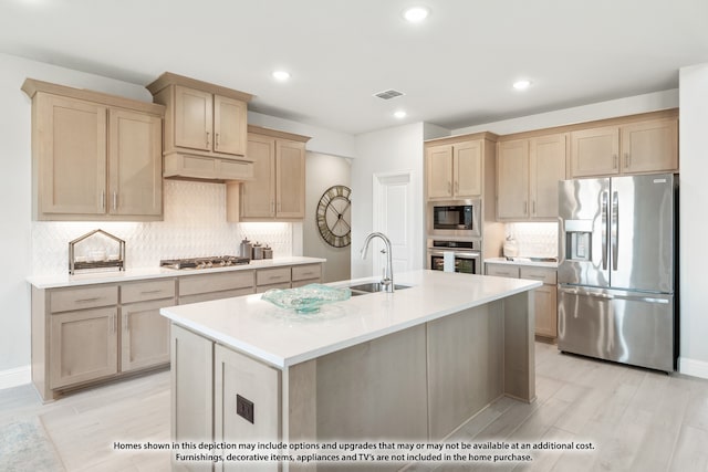 kitchen featuring tasteful backsplash, stainless steel appliances, light brown cabinetry, and an island with sink