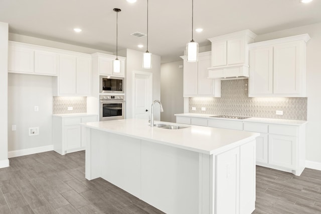 kitchen featuring light countertops, white cabinetry, a sink, an island with sink, and oven