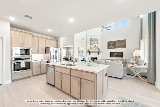 kitchen with stainless steel appliances, a kitchen island with sink, light wood-type flooring, a large fireplace, and sink