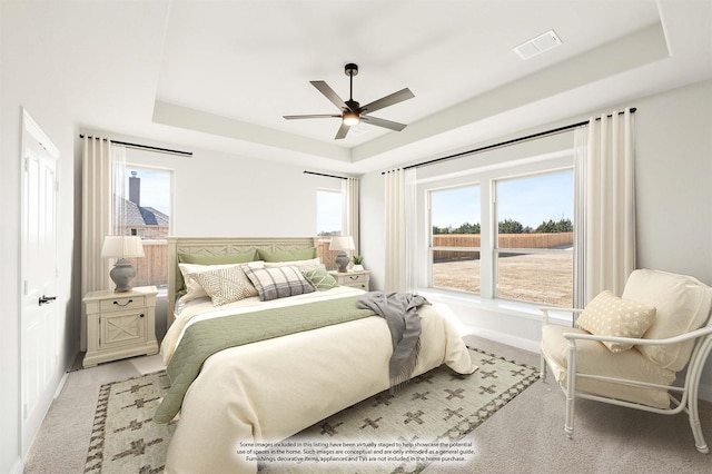 bedroom featuring ceiling fan, a tray ceiling, visible vents, and light colored carpet