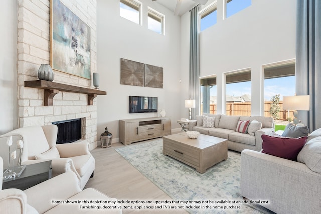 living room featuring a towering ceiling, a healthy amount of sunlight, a fireplace, and light hardwood / wood-style floors