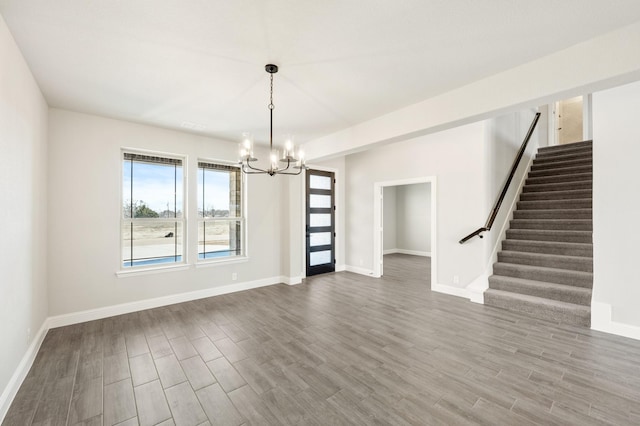 empty room with baseboards, stairway, an inviting chandelier, and wood finished floors