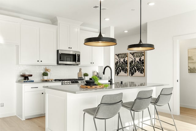 kitchen with decorative backsplash, stove, an island with sink, and light hardwood / wood-style floors