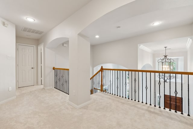 hallway with a notable chandelier, crown molding, and carpet flooring