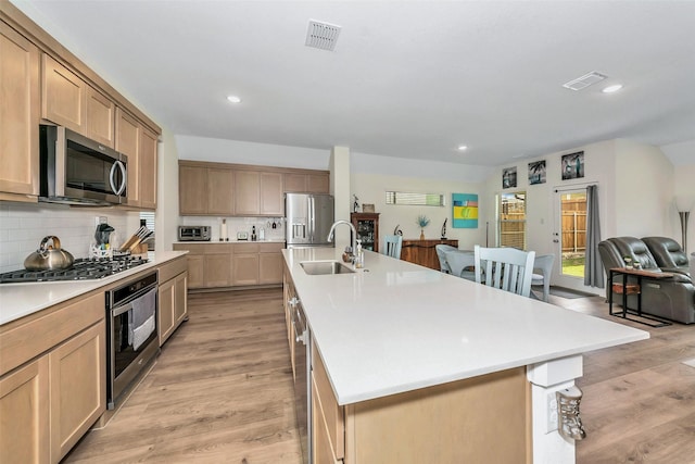 kitchen featuring tasteful backsplash, light wood-style flooring, appliances with stainless steel finishes, open floor plan, and a sink