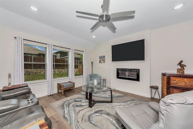 living room with recessed lighting, wood finished floors, baseboards, vaulted ceiling, and a glass covered fireplace