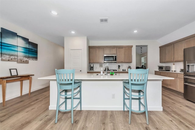 kitchen with a kitchen island with sink, stainless steel appliances, visible vents, light countertops, and light wood finished floors