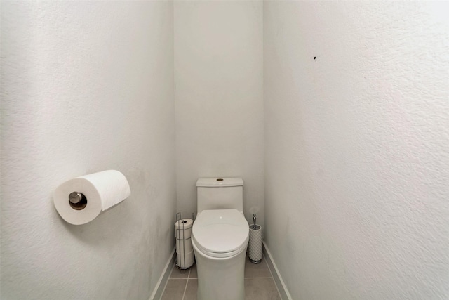 bathroom featuring a textured wall, tile patterned flooring, toilet, and baseboards