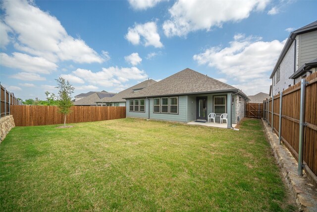 rear view of property featuring a patio area, a fenced backyard, a lawn, and roof with shingles