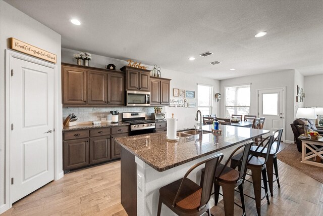 kitchen with a breakfast bar, appliances with stainless steel finishes, sink, and light hardwood / wood-style floors