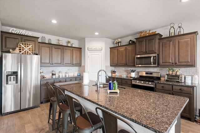 kitchen with appliances with stainless steel finishes, light hardwood / wood-style flooring, and an island with sink