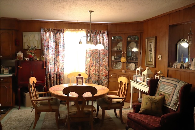 dining area with a textured ceiling, carpet floors, wooden walls, and an inviting chandelier