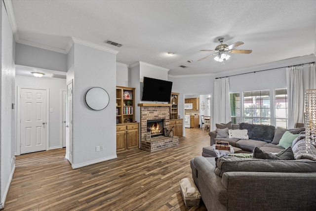 living room with a fireplace, dark hardwood / wood-style flooring, a textured ceiling, ornamental molding, and ceiling fan