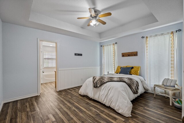 bedroom with ceiling fan, a raised ceiling, hardwood / wood-style flooring, and ensuite bath