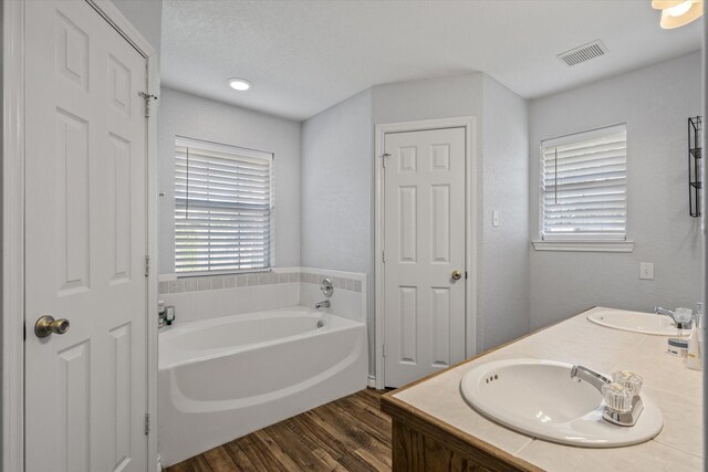 bathroom with hardwood / wood-style floors, dual bowl vanity, a tub to relax in, and a textured ceiling