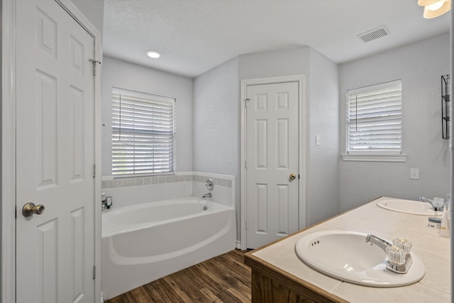 bathroom featuring a bath, wood finished floors, a sink, and visible vents