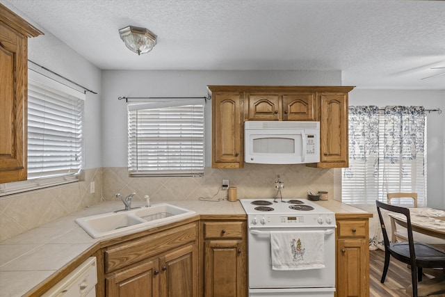 kitchen featuring a textured ceiling, light wood-type flooring, white appliances, sink, and tile countertops