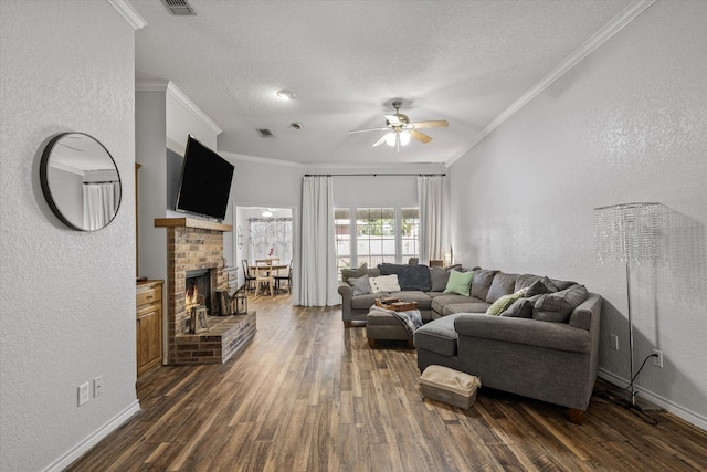 living room featuring dark wood-type flooring, a textured ceiling, ceiling fan, ornamental molding, and a fireplace