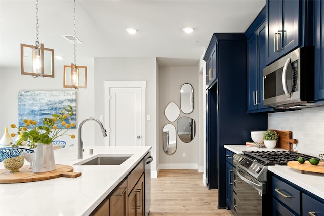 kitchen featuring light wood-type flooring, stainless steel appliances, sink, blue cabinetry, and hanging light fixtures