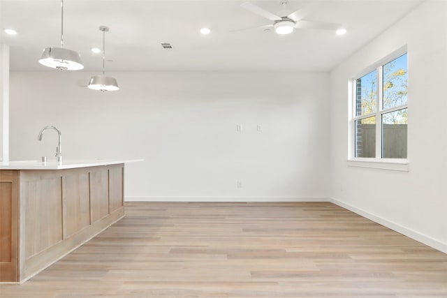 interior space featuring an island with sink, light hardwood / wood-style flooring, hanging light fixtures, and ceiling fan