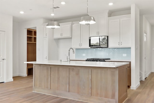 kitchen featuring pendant lighting, stainless steel appliances, white cabinetry, and a center island with sink