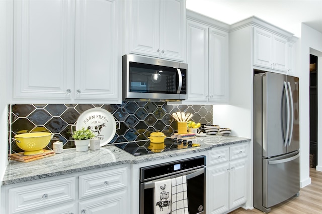 kitchen with light hardwood / wood-style flooring, white cabinetry, appliances with stainless steel finishes, light stone countertops, and tasteful backsplash