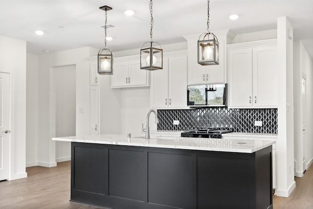 kitchen with sink, white cabinetry, light stone counters, decorative light fixtures, and a center island with sink