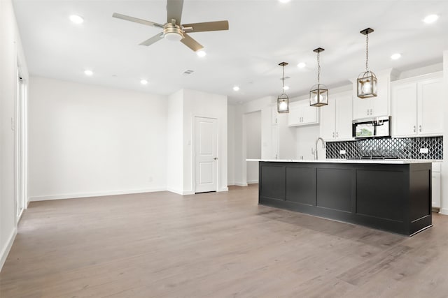 kitchen with light wood-type flooring, an island with sink, hanging light fixtures, and white cabinets