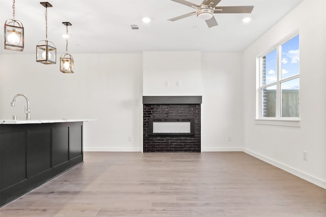 unfurnished living room featuring a healthy amount of sunlight, a brick fireplace, sink, and light hardwood / wood-style floors