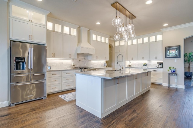 kitchen with high quality fridge, a sink, white cabinetry, glass insert cabinets, and custom range hood