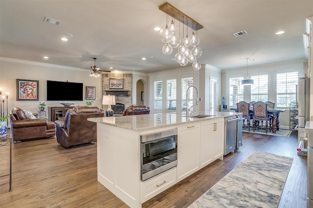 kitchen featuring a kitchen island with sink, a sink, white cabinetry, light stone countertops, and decorative light fixtures