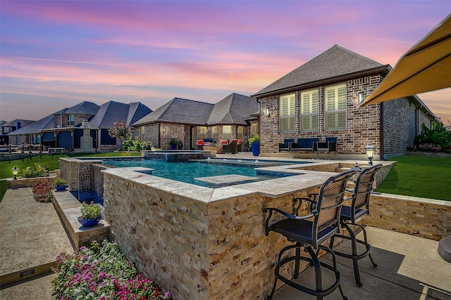 pool at dusk featuring outdoor dry bar, a pool with connected hot tub, fence, a residential view, and a patio