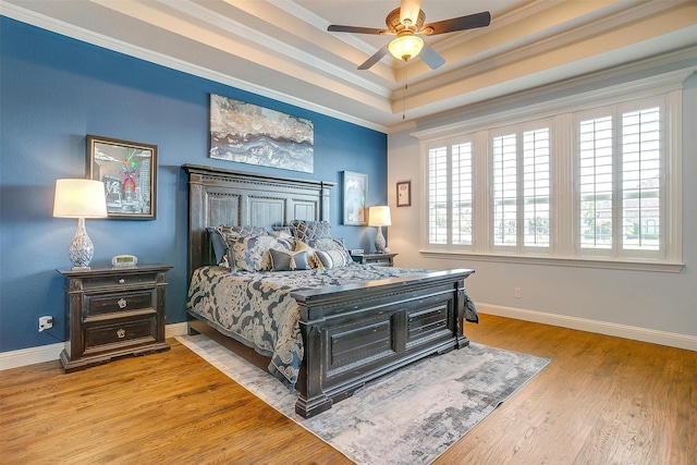 bedroom with light wood finished floors, baseboards, a raised ceiling, and crown molding