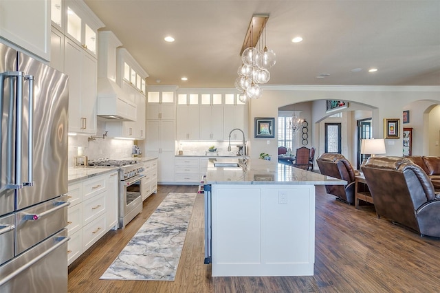 kitchen with high end appliances, arched walkways, a sink, open floor plan, and tasteful backsplash