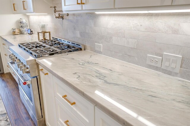 kitchen with light stone counters, stainless steel stove, white cabinets, dark wood-type flooring, and backsplash