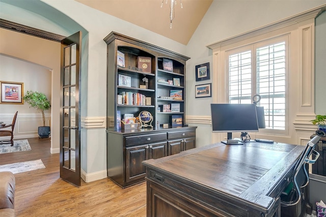 office area featuring lofted ceiling, light wood-style flooring, wainscoting, and a decorative wall