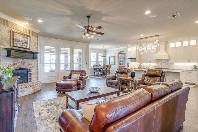 living room with visible vents, a ceiling fan, crown molding, light wood-style floors, and a fireplace