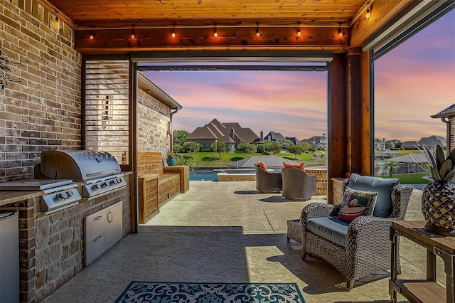 patio terrace at dusk featuring area for grilling and exterior kitchen